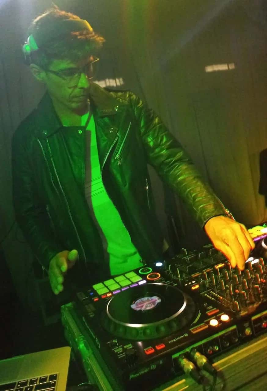 DJ BetoBrizz mixando em uma controladora Pioneer com fones de ouvido sob luz verde