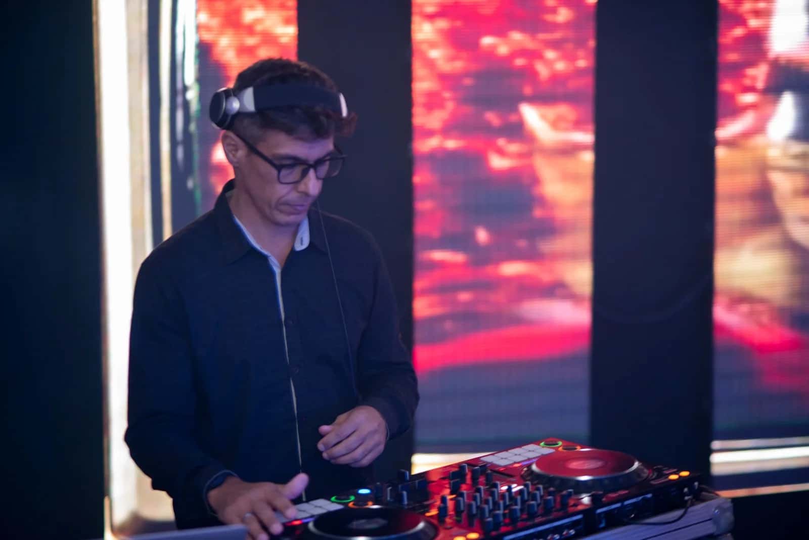 DJ BetoBrizz mixando na controladora diante de telões de LED com visuais vermelhos